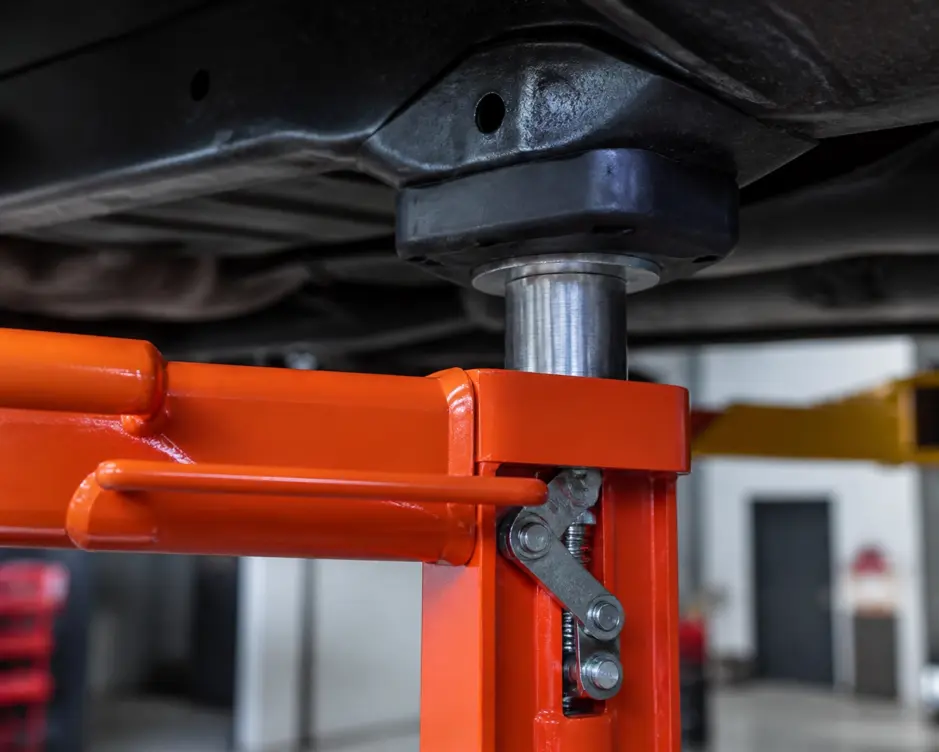 Close-up of a 2 post car lift arm with safety lock engaged and adapter pad on a vehicle frame lift point