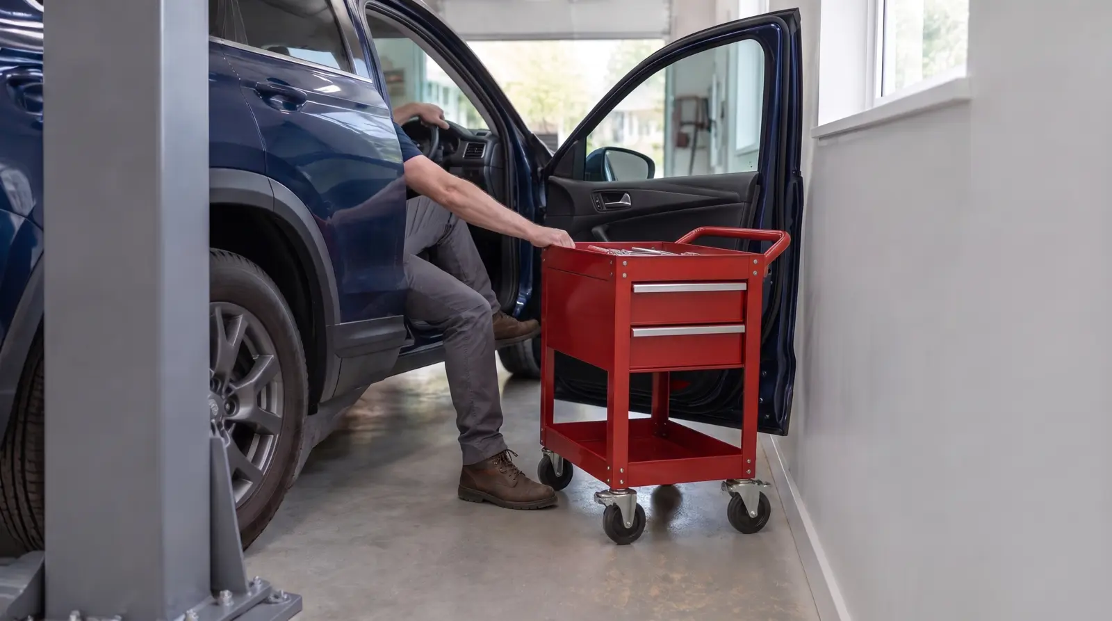 Open driver door beside a 2 post lift column with a tool cart passing between the vehicle and the side wall